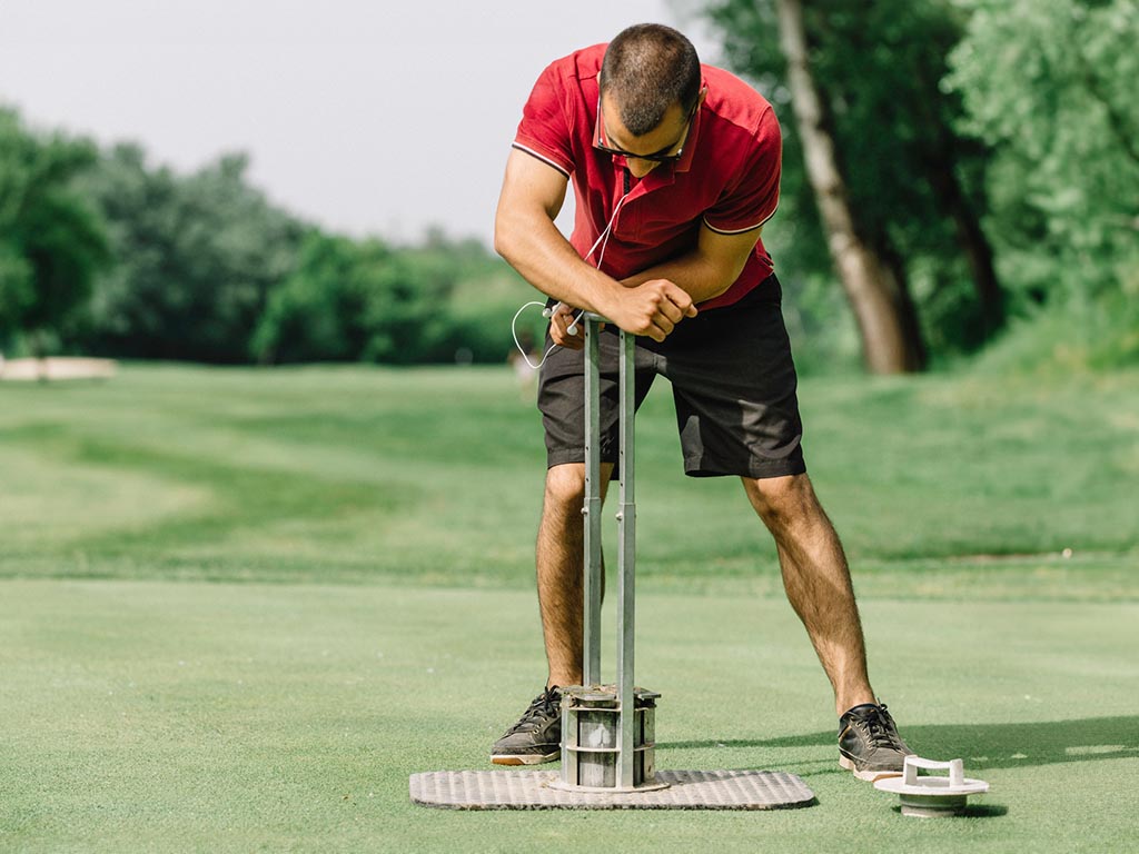 Greenskeeper cutting a golf hole in the putting green.